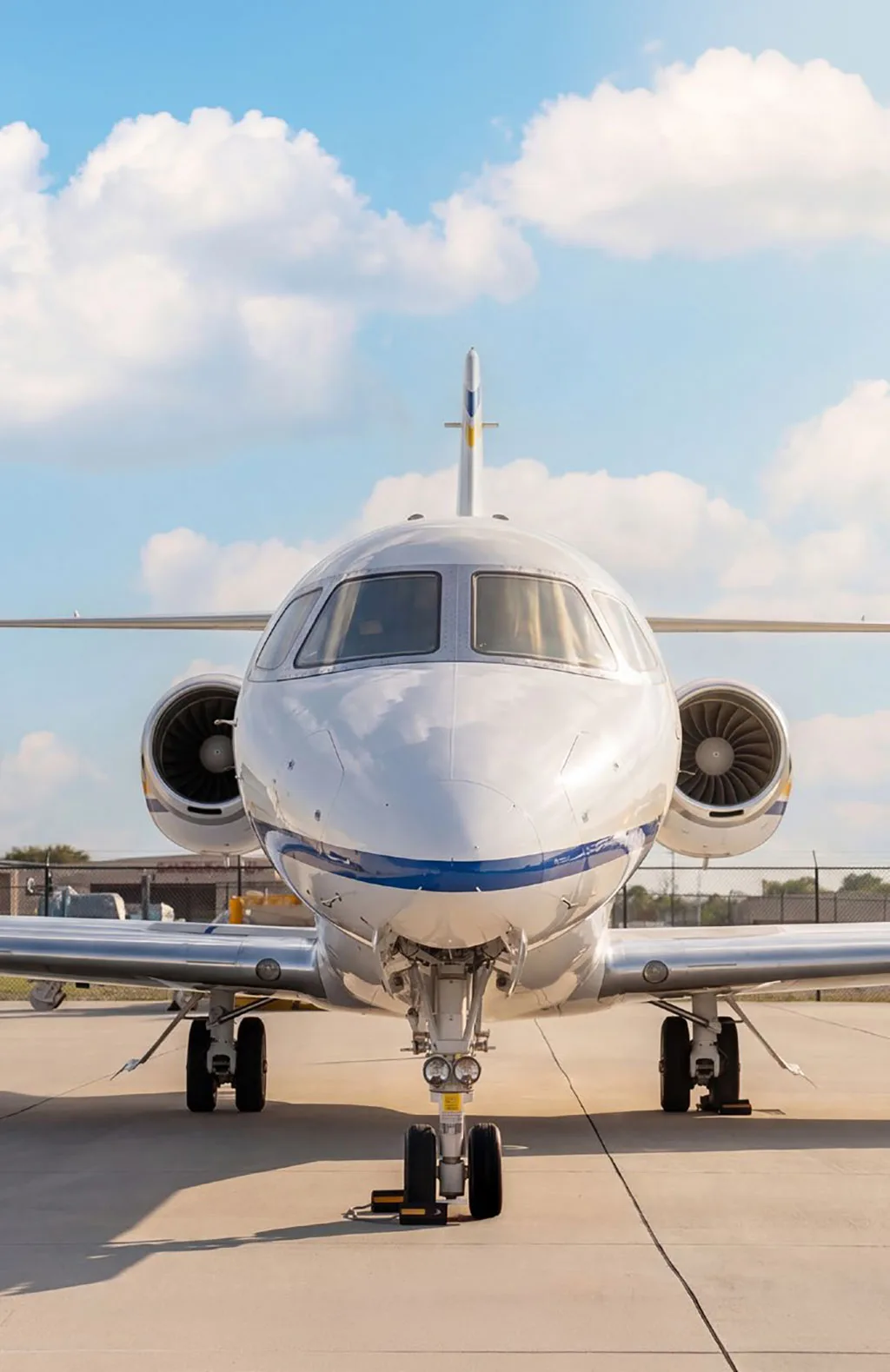 A head-on view of a white Cessna Citation Latitude business jet with blue stripes on the nose, parked on a tarmac.