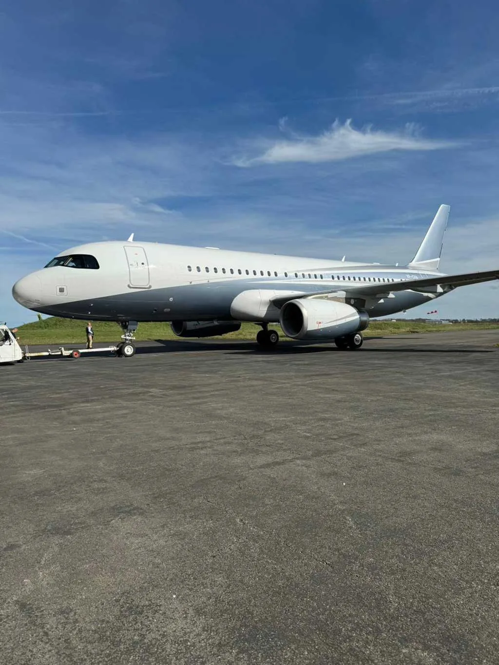 A large white and grey private jet is parked on an asphalt tarmac under a blue sky.