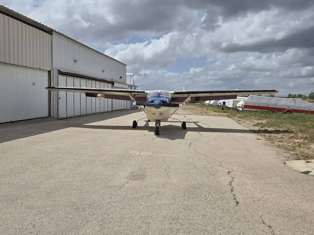 A cream, blue, and maroon Cessna 337 Skymaster parked head-on in front of a hangar.