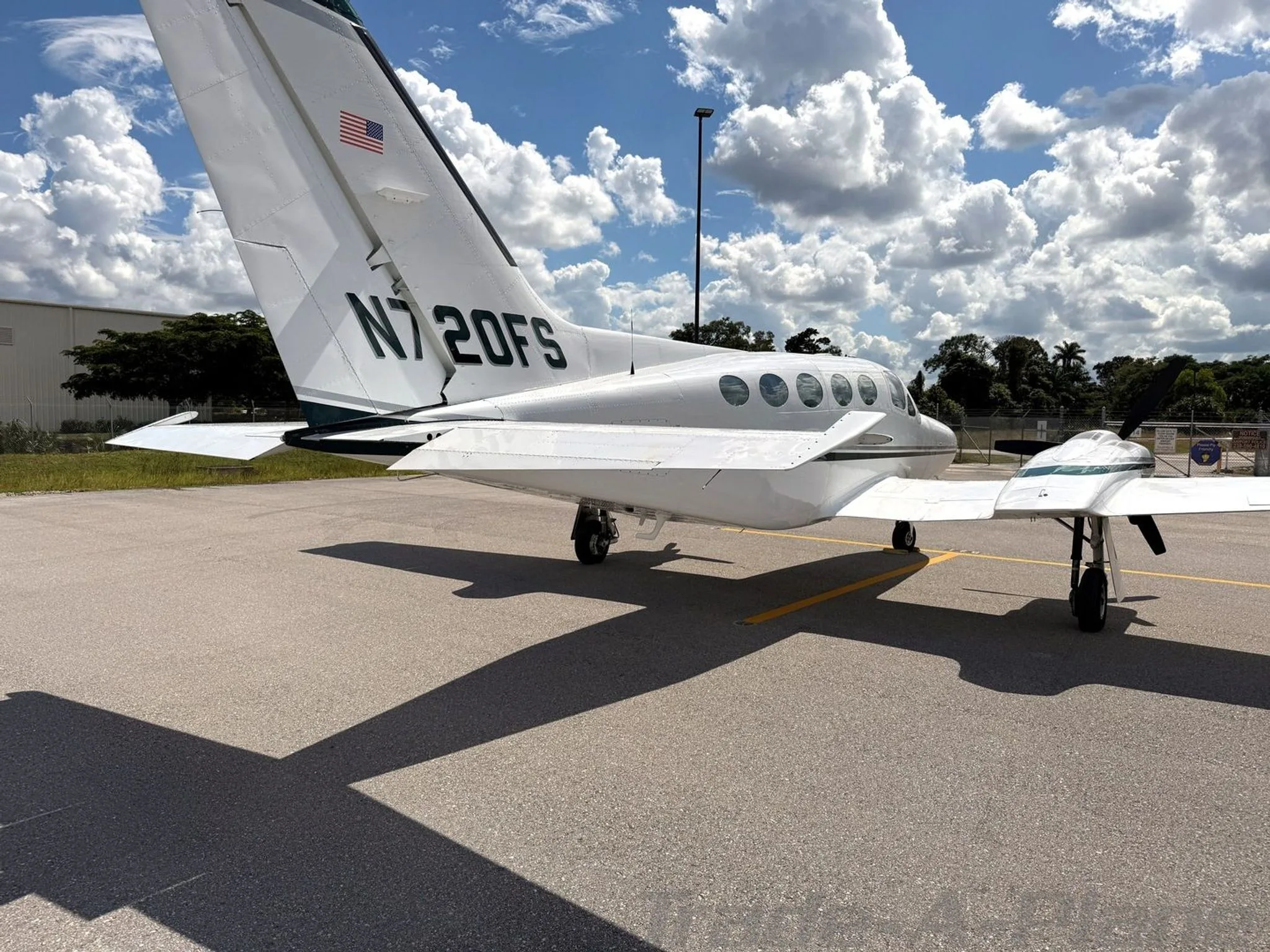 A white Cessna 414 Chancellor aircraft, N720FS, with dark green stripes, parked on an airfield, viewed from the rear left showing the tail and right wing.