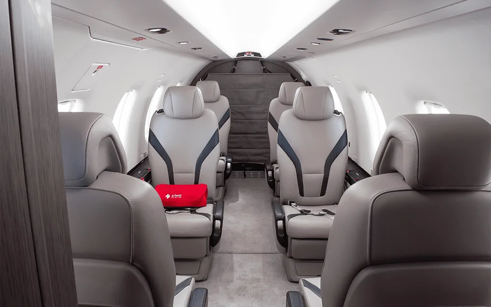 A view down the aisle of the Pilatus PC-12 cabin, showing light grey passenger seats with black accents.