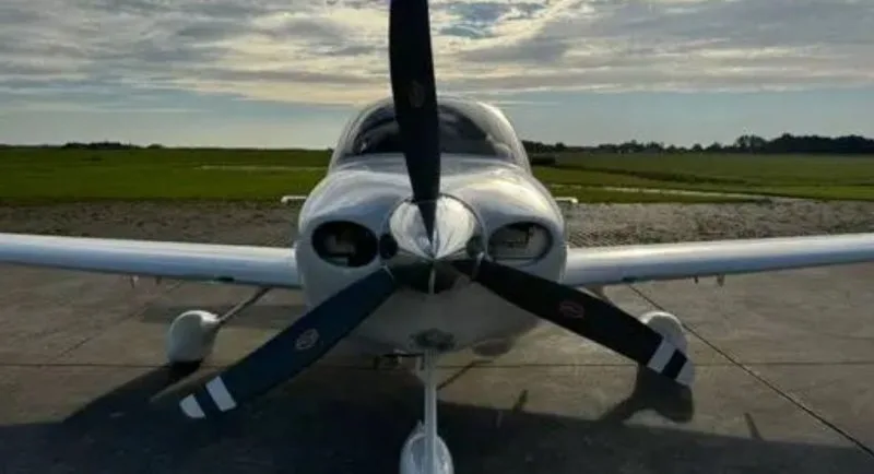A head-on view of a white Cirrus SR20 aircraft with its propeller, parked on a tarmac.