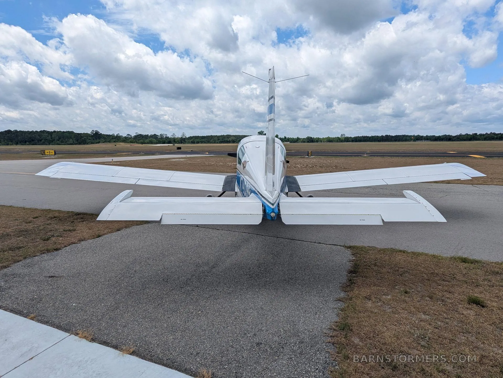 A rear view of a white and blue Grumman AA-5 aircraft with registration N74099 parked on an airfield.