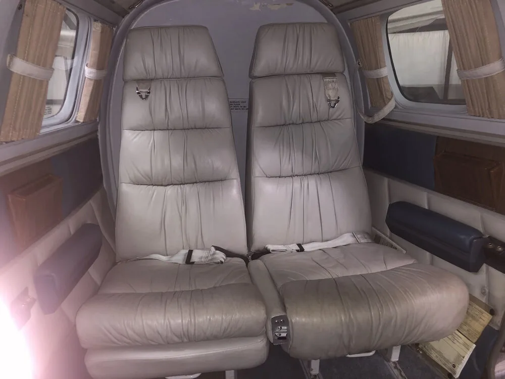 Two rows of light grey leather passenger seats inside an aircraft cabin with small windows and brown curtains.