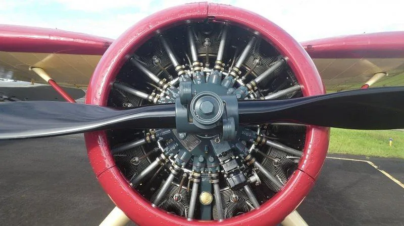 A close-up view of the radial engine and propeller of a vintage aircraft, with a red cowling.