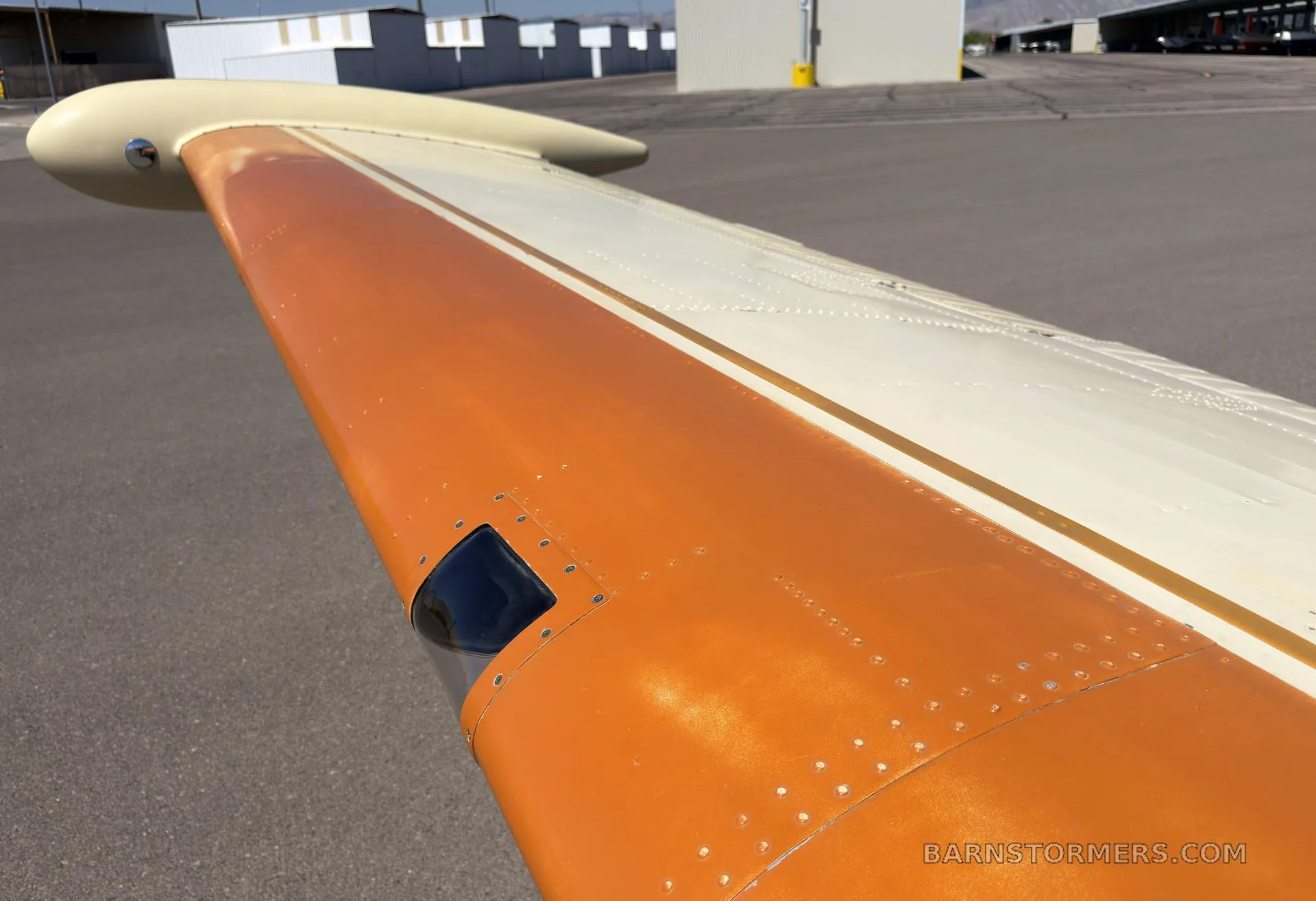 A close-up view of the orange and cream wing of a single-engine aircraft, showing rivets and a navigation light.