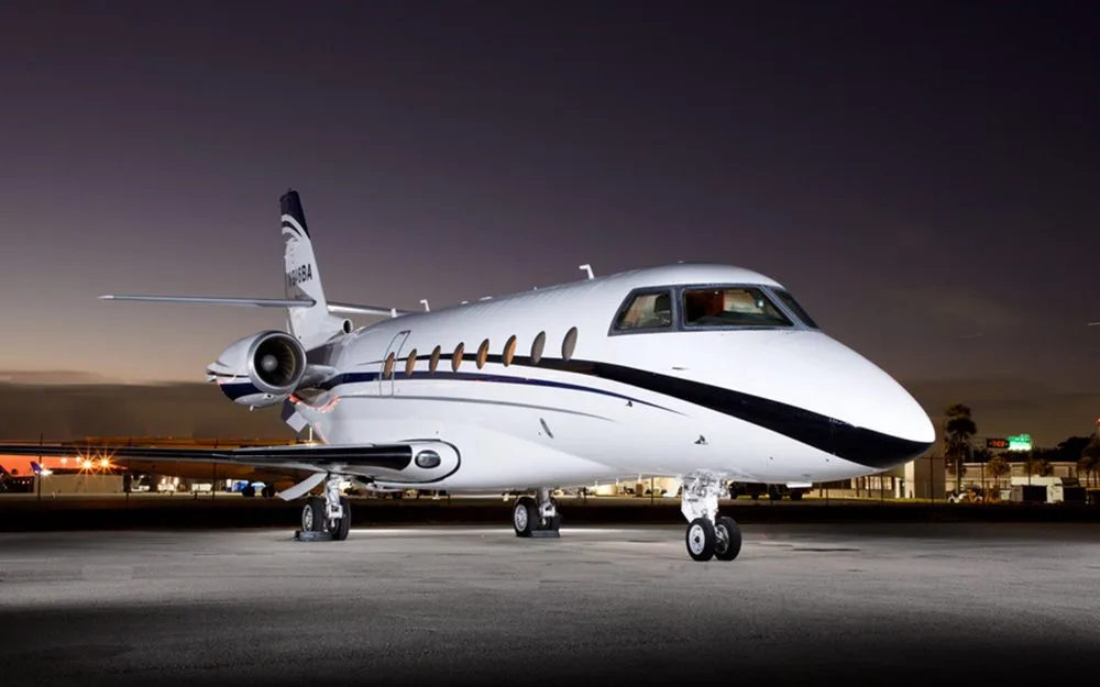 A white business jet with blue and black stripes, registration N946BA, parked on an airfield at night, viewed from the front-right.