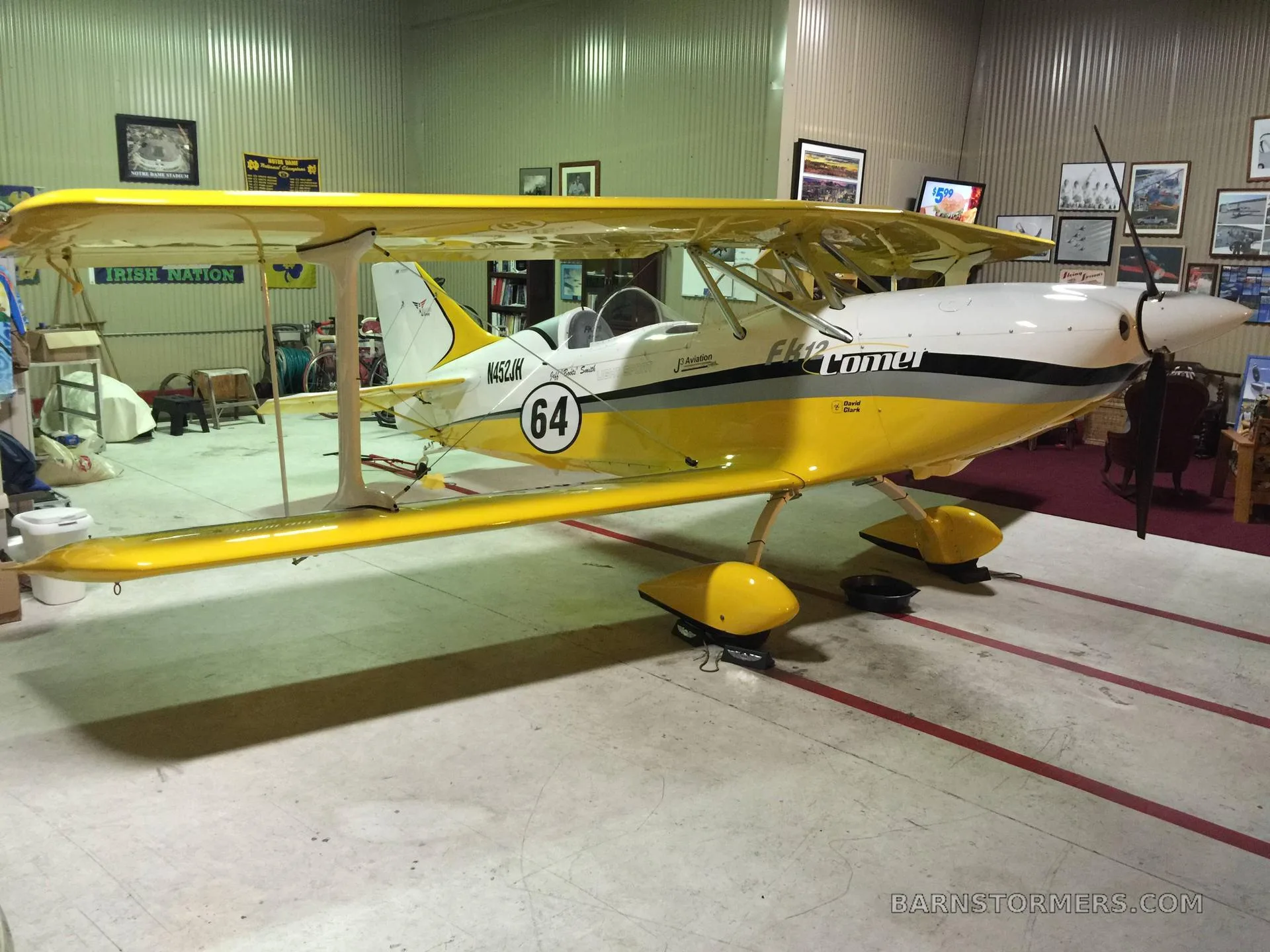 A yellow and white FK12 Comet biplane with '64' on the tail, parked in a hangar.