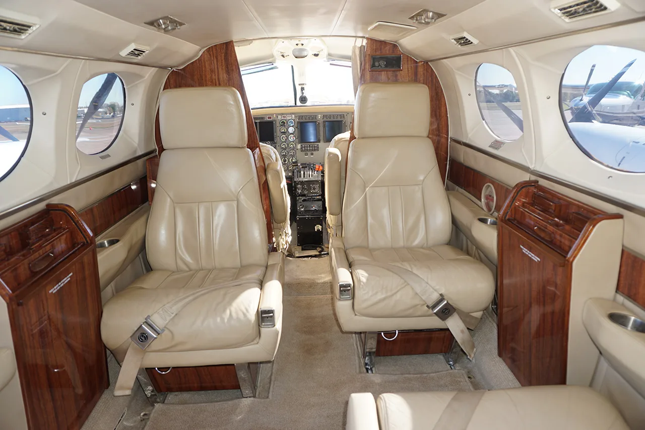 Interior view of the aircraft cabin with tan leather seats, wood trim, and a glimpse of the cockpit.