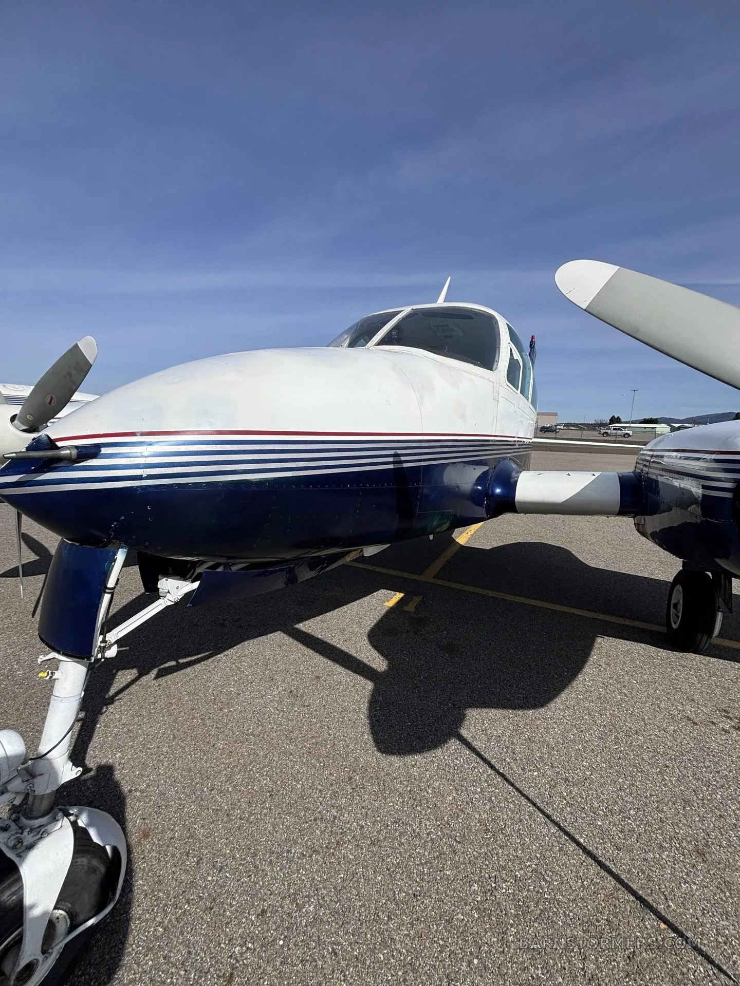 A close-up, low-angle view of the front of a white and blue Cessna 310I, registration N27ZZ, parked on an airfield.