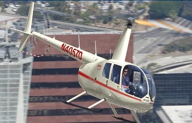 A white Robinson R44 helicopter with red stripes and tail number N40570 flies over a city.