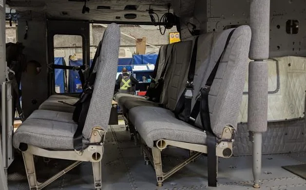 Two rows of grey fabric passenger seats with seatbelts are visible inside a helicopter cabin.