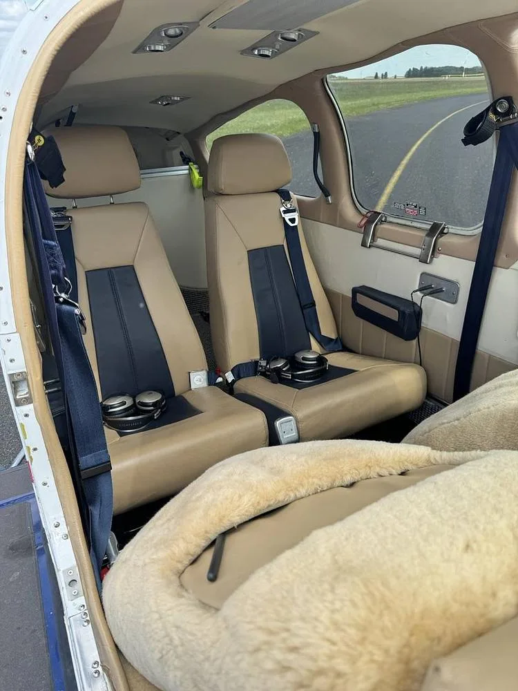 The tan and blue leather interior cabin seats of a small aircraft, with a furry cover on the front seat.