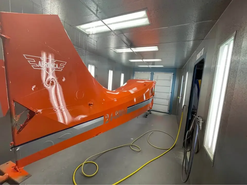 The orange fuselage and tail of an Aeronca aircraft, with tail number 24-8804, in a brightly lit paint booth.