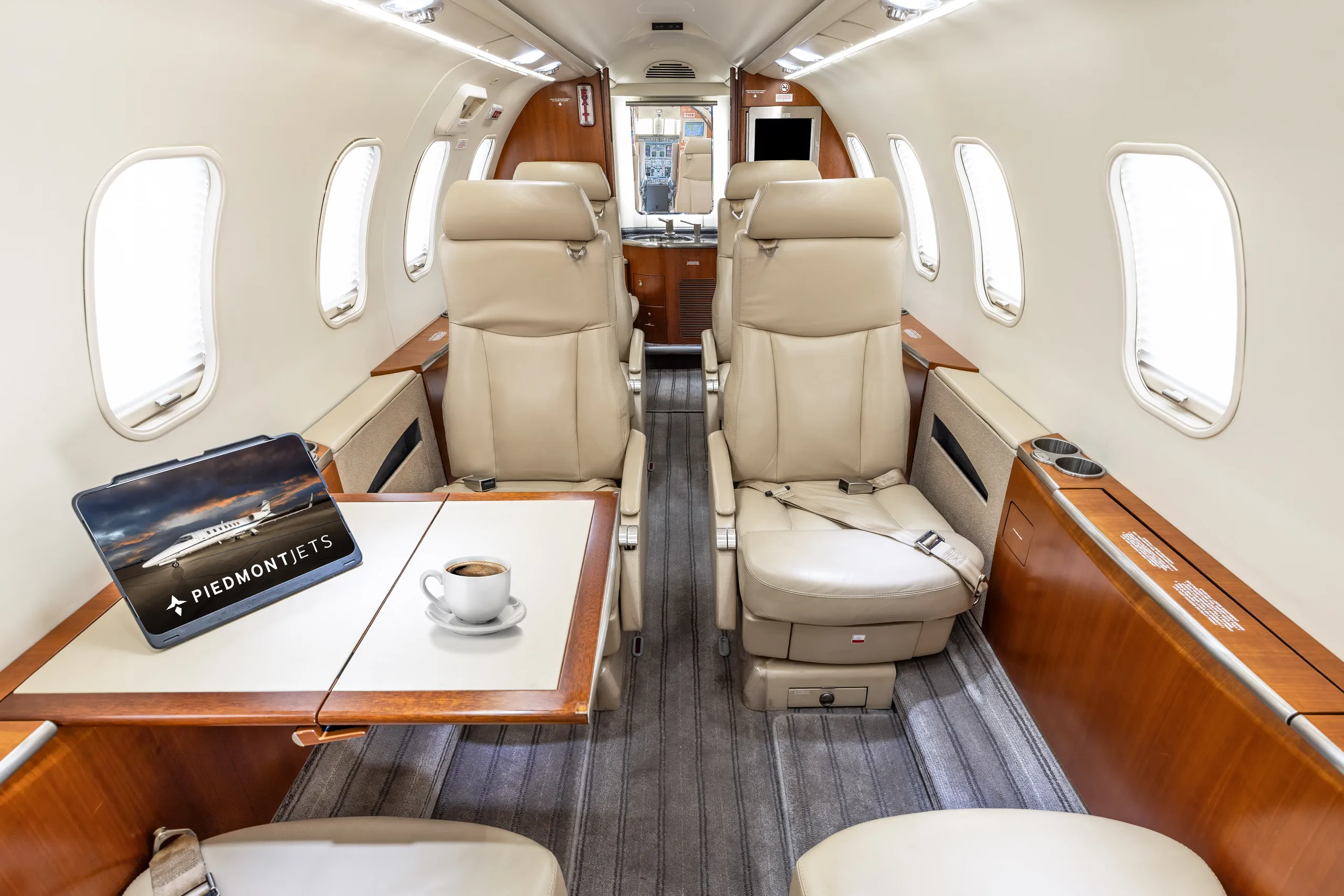 Aircraft cabin interior showing beige seats, a table with a coffee cup, and a tablet displaying "Piedmont Jets".
