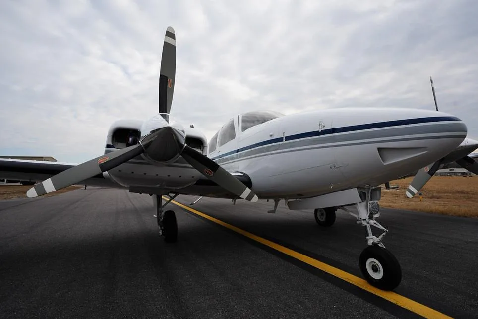 A low-angle front-right view of a white twin-engine propeller aircraft with blue and grey stripes on an asphalt surface.