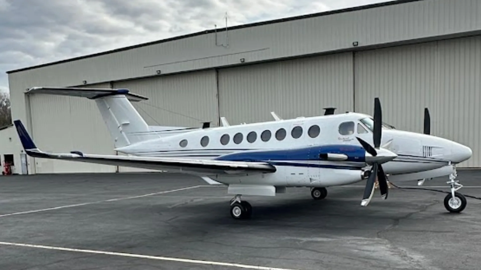 A white and blue Beechcraft King Air N506KB is parked on an asphalt ramp in front of a hangar.