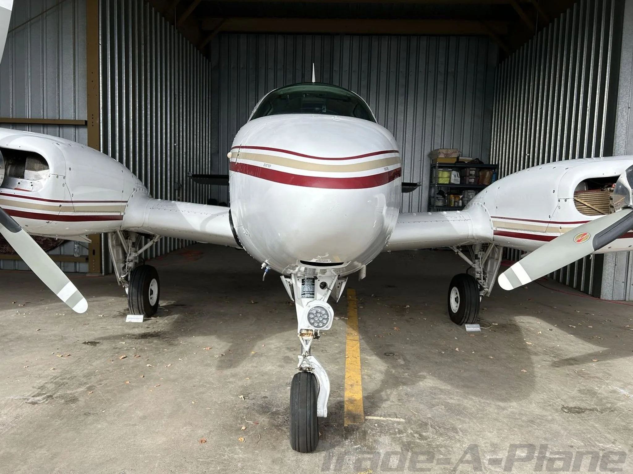 A head-on view of the white and maroon Beechcraft Baron N29SF parked inside a hangar.