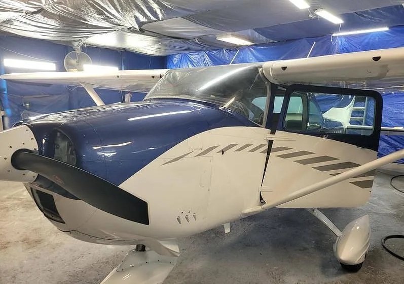 A front-quarter view of the blue and white Cessna N4303S with an open door in a hangar.