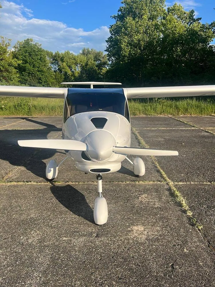 Front view of a white Alpha Light Sport aircraft with a propeller, parked on a concrete surface.