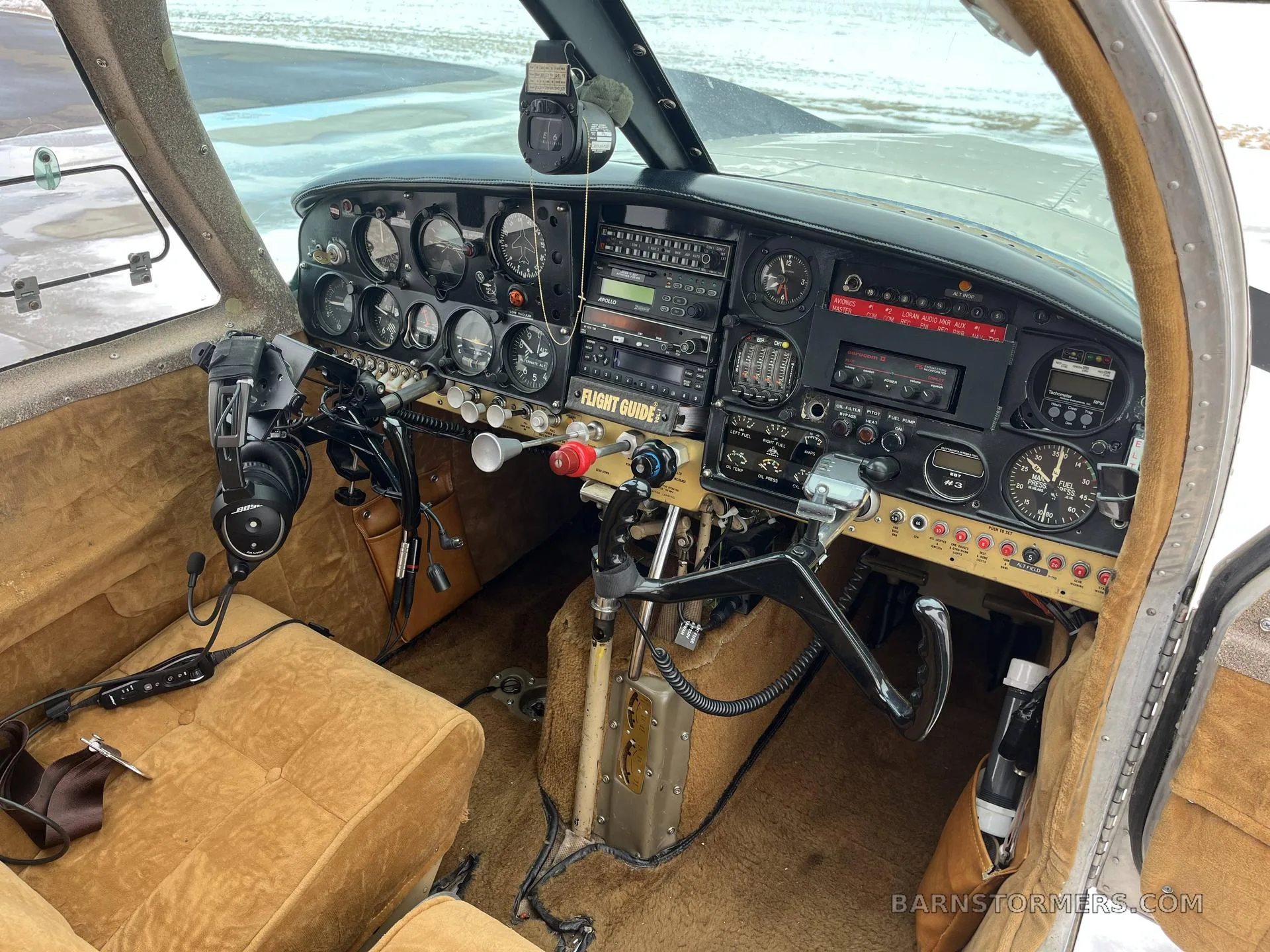 The aircraft's cockpit shows the instrument panel, controls, and tan upholstered seats.