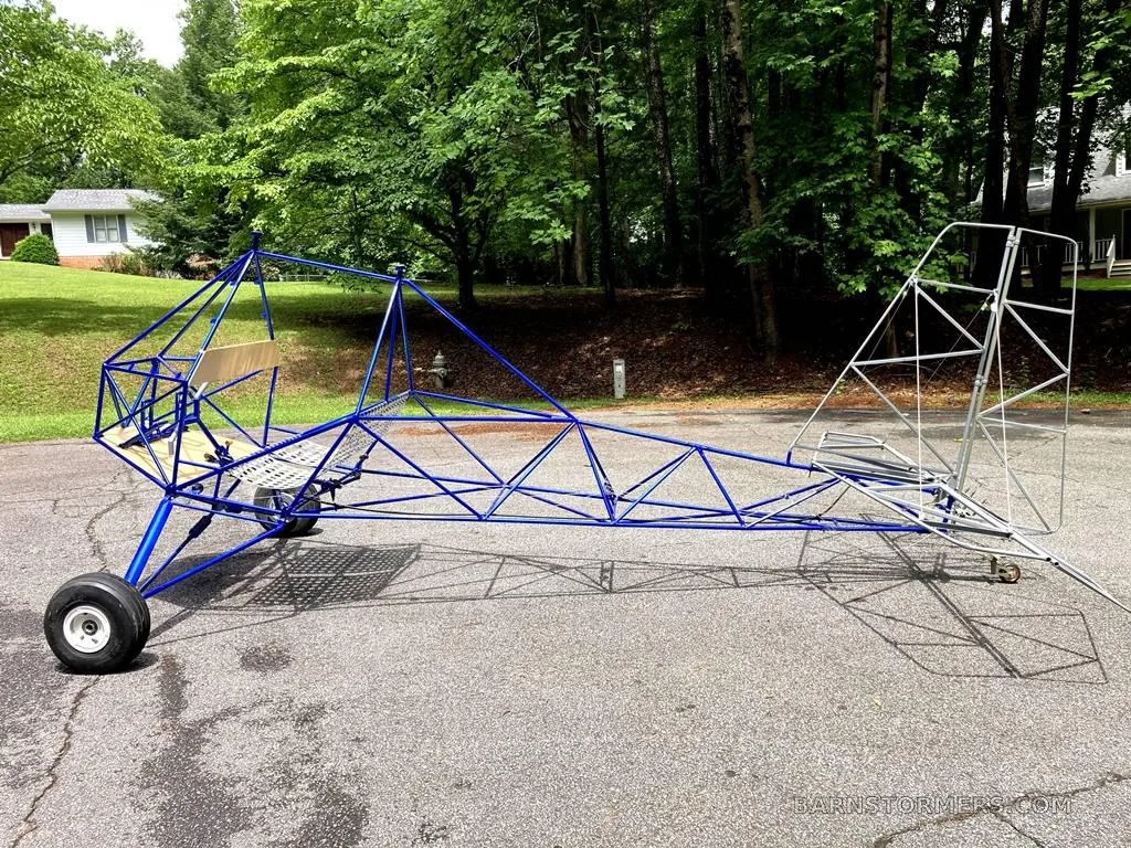 A blue and white ultralight aircraft frame with landing gear sits on a paved driveway.