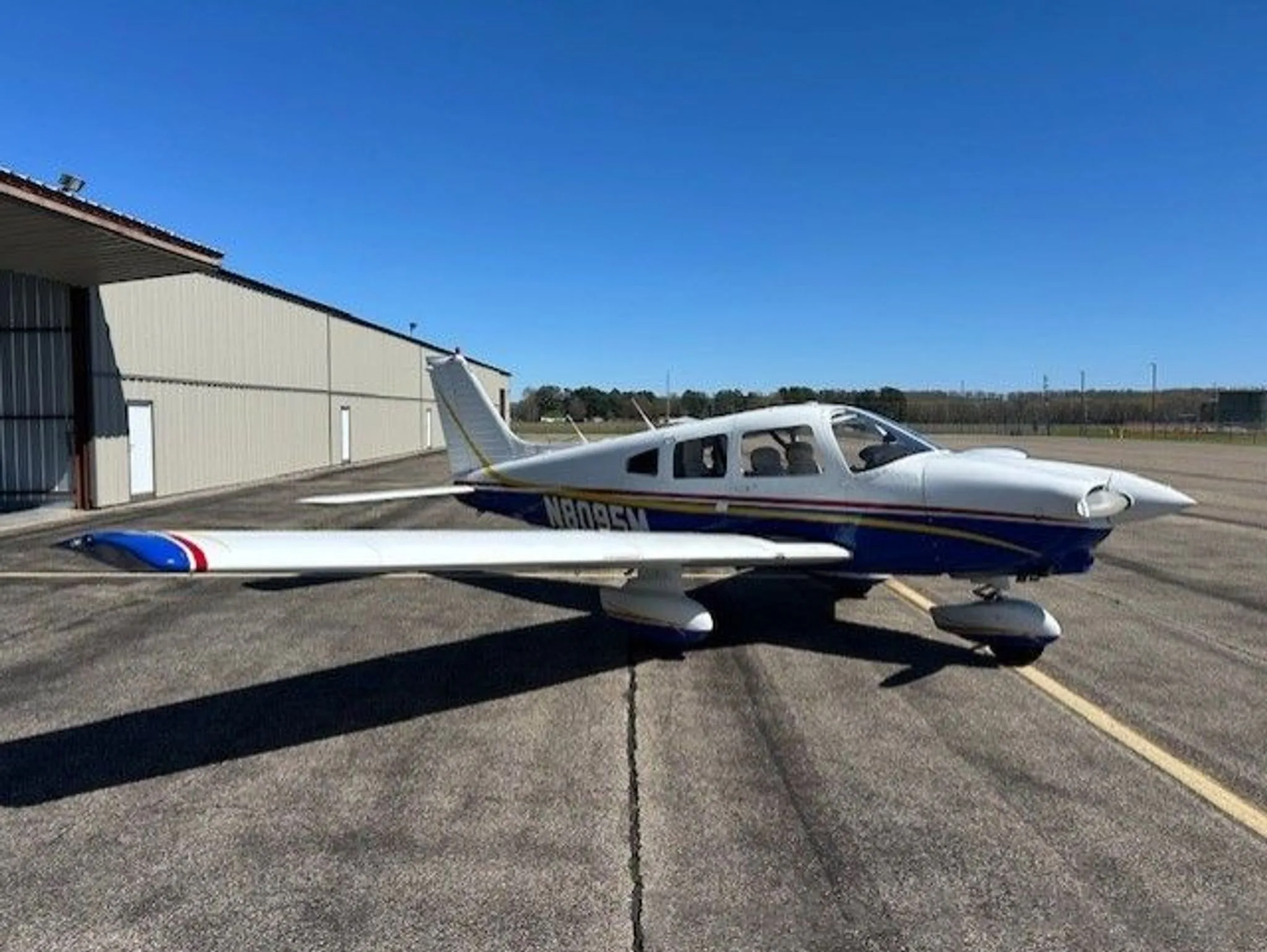 A side view of a white and blue Piper Cherokee aircraft with N8095M registration parked on an airfield.