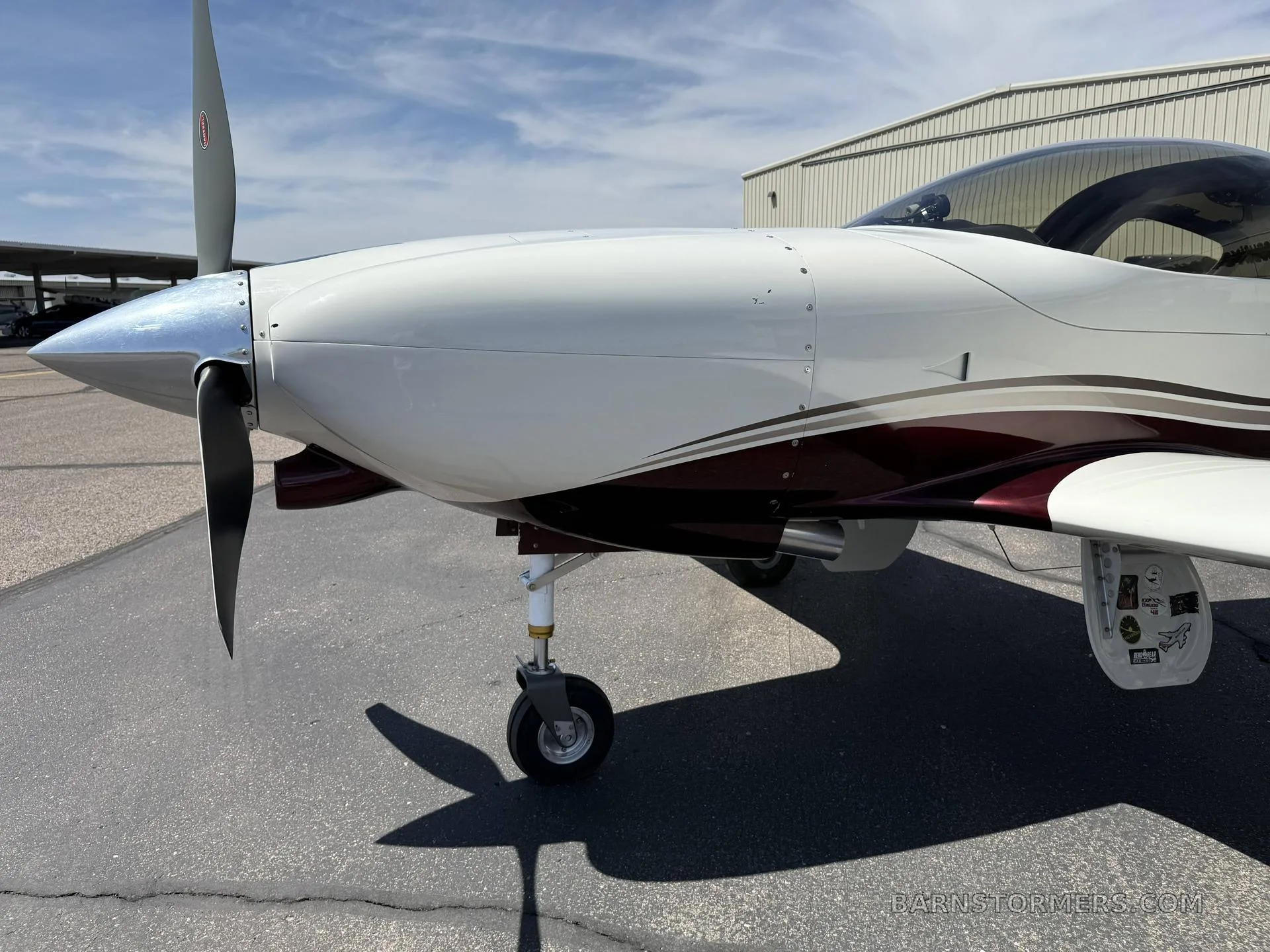 A close-up view of the nose and propeller of a white and maroon single-engine aircraft (N49LJ) on an asphalt apron.