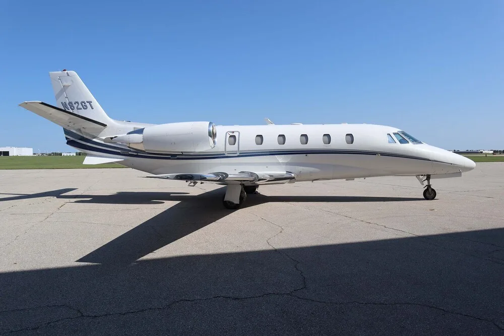 A white Cessna Citation business jet with blue and grey stripes, registration N82GT, parked on a tarmac under a clear blue sky.