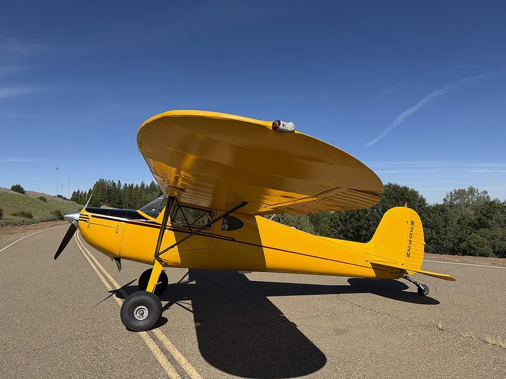 A bright yellow high-wing aircraft, registration N2092N, parked on an asphalt surface with trees and hills in the background.