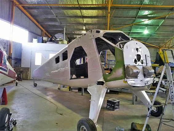 The white fuselage of an aircraft, partially assembled, sitting on landing gear in a hangar.