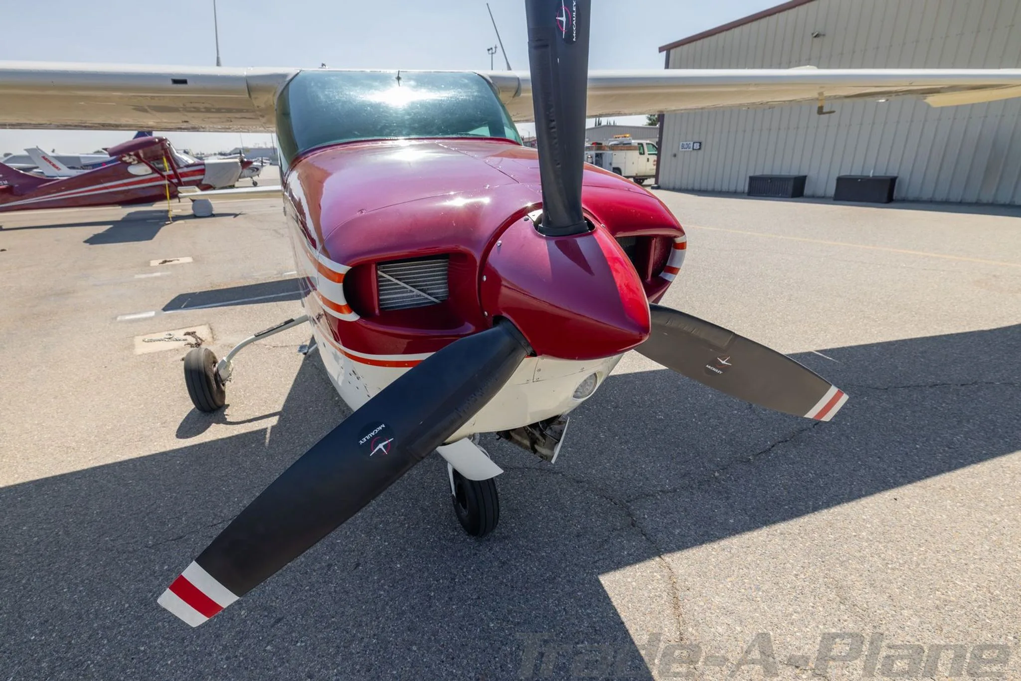 A front view of the red nose and propeller of a Cessna 210 Centurion aircraft parked on an airfield.