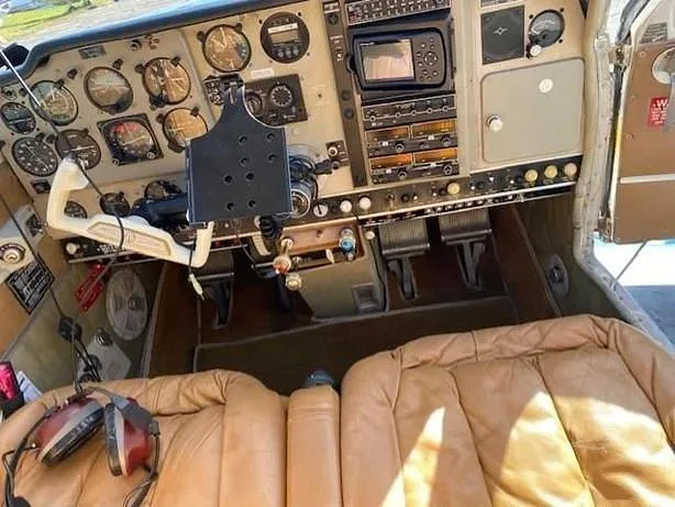The cockpit of a small aircraft with analog gauges, a GPS unit, and tan leather seats.