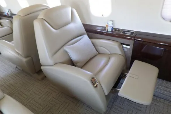 A close-up view of a beige leather seat with a footrest in a private jet cabin.