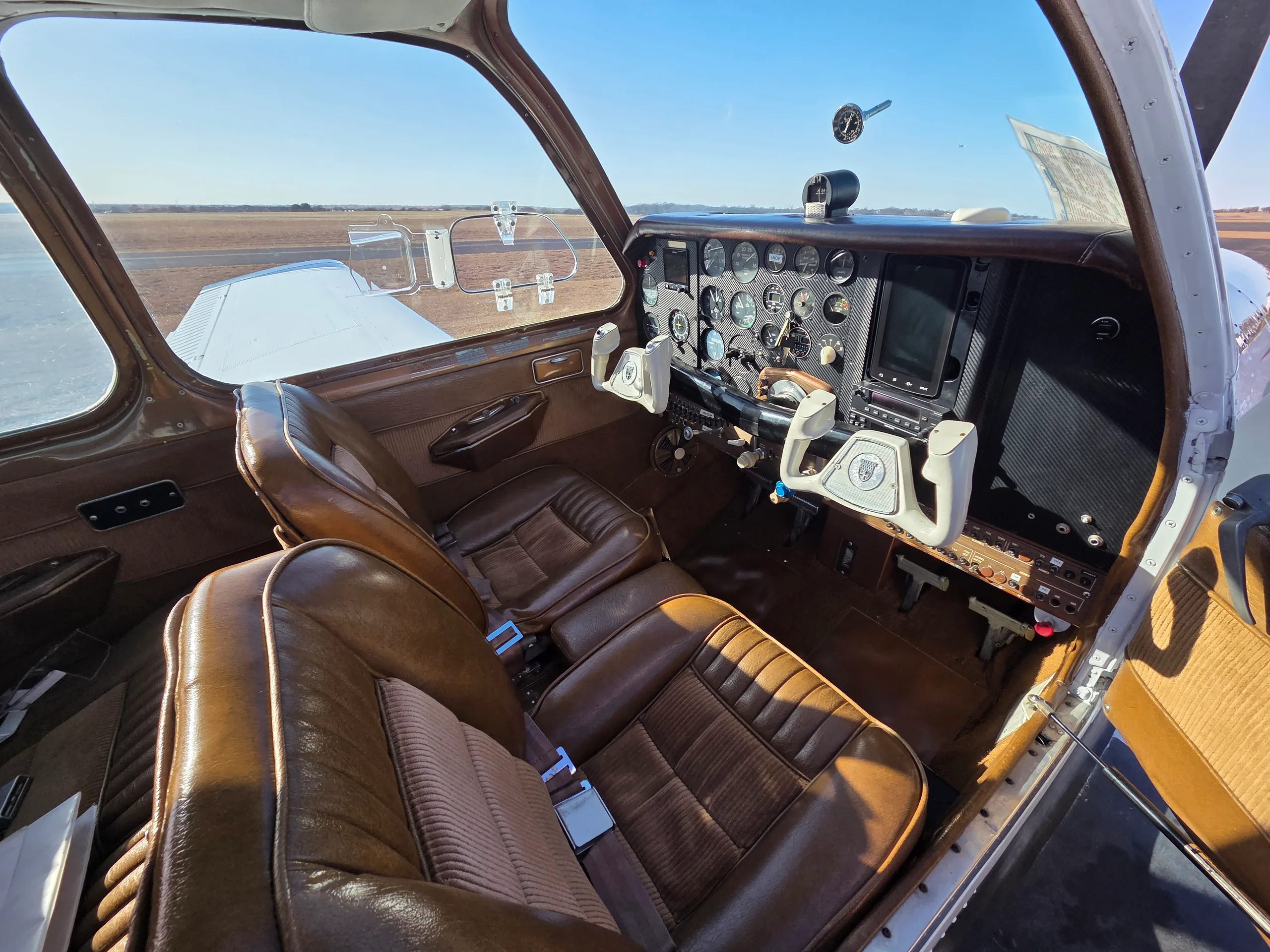 The cockpit and cabin interior of a small aircraft, featuring brown leather seats and a classic instrument panel.