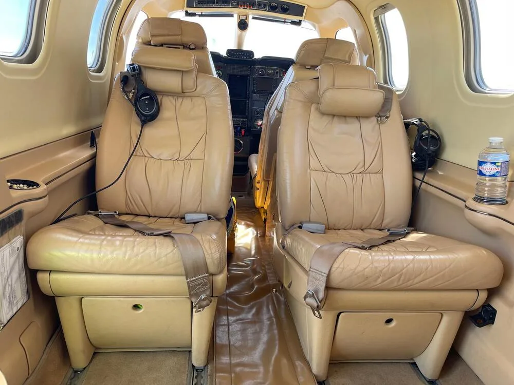 The tan leather interior cabin of an aircraft, showing two forward-facing seats and a view into the cockpit.