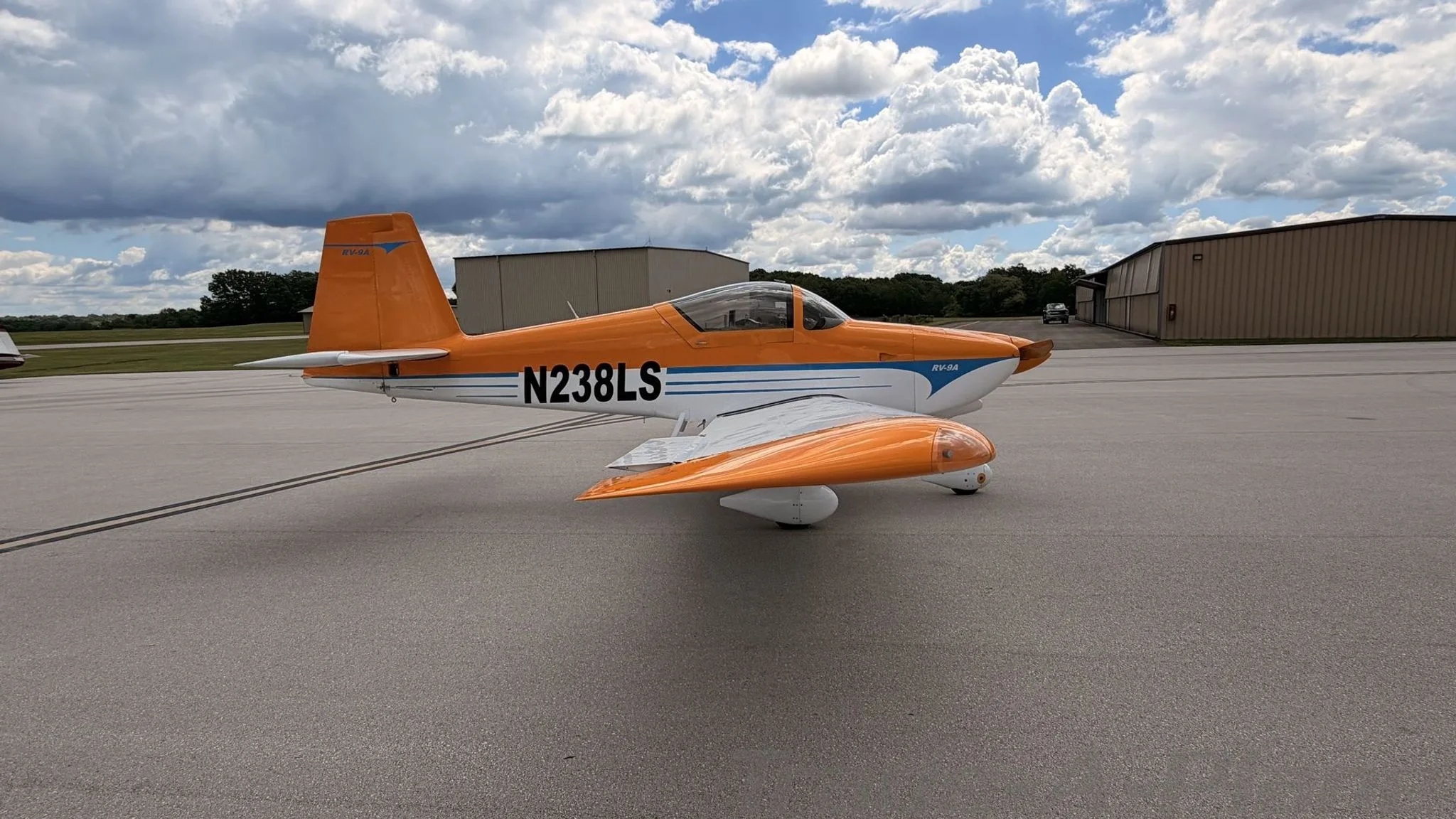 The aircraft is shown from the side with hangars in the background.