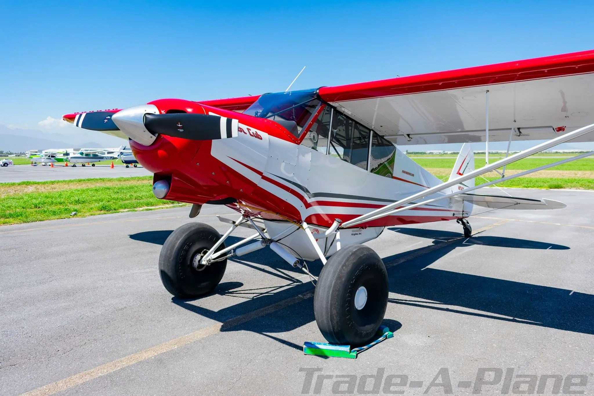 A close-up front view of the propeller and nose of a red and white Super Cub aircraft on an airfield.