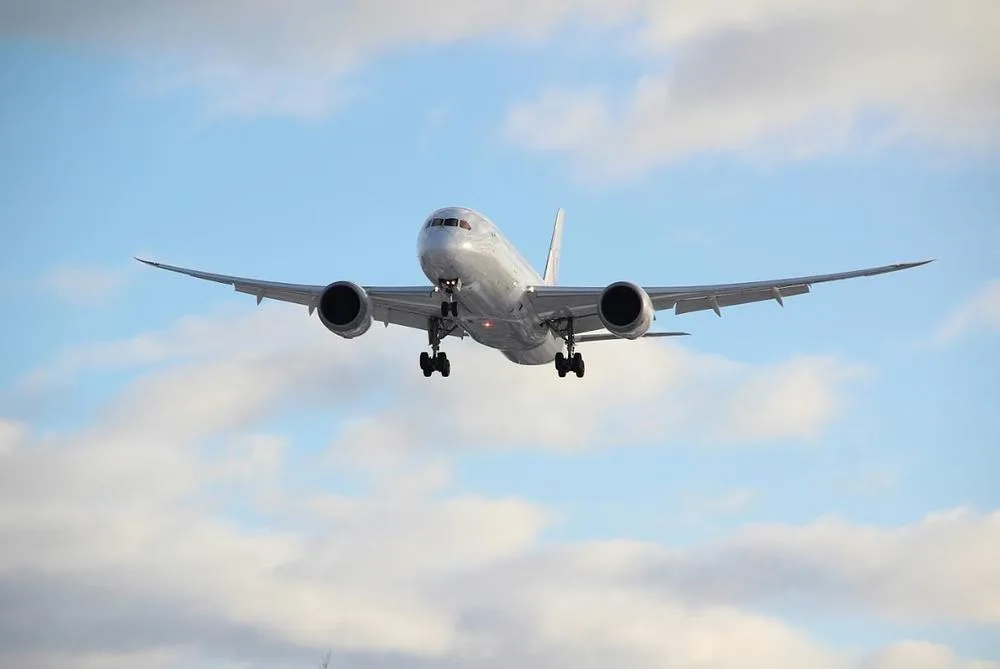 A white Boeing 787 Dreamliner with landing gear extended approaches for landing against a cloudy blue sky.