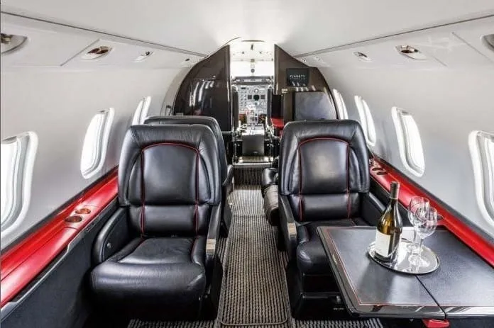 The luxurious interior cabin of a private jet with black leather seats and a table set with wine.