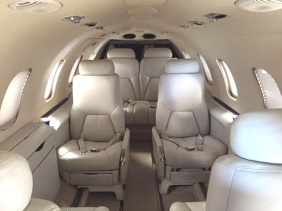The interior of a private jet cabin with light-colored leather seats arranged facing each other.