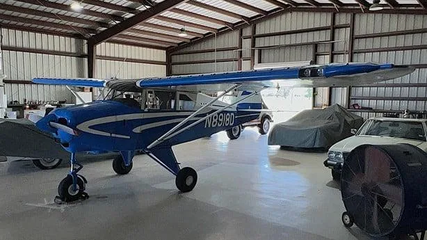 A blue and white single-engine aircraft, N8918D, parked in a hangar with other vehicles.