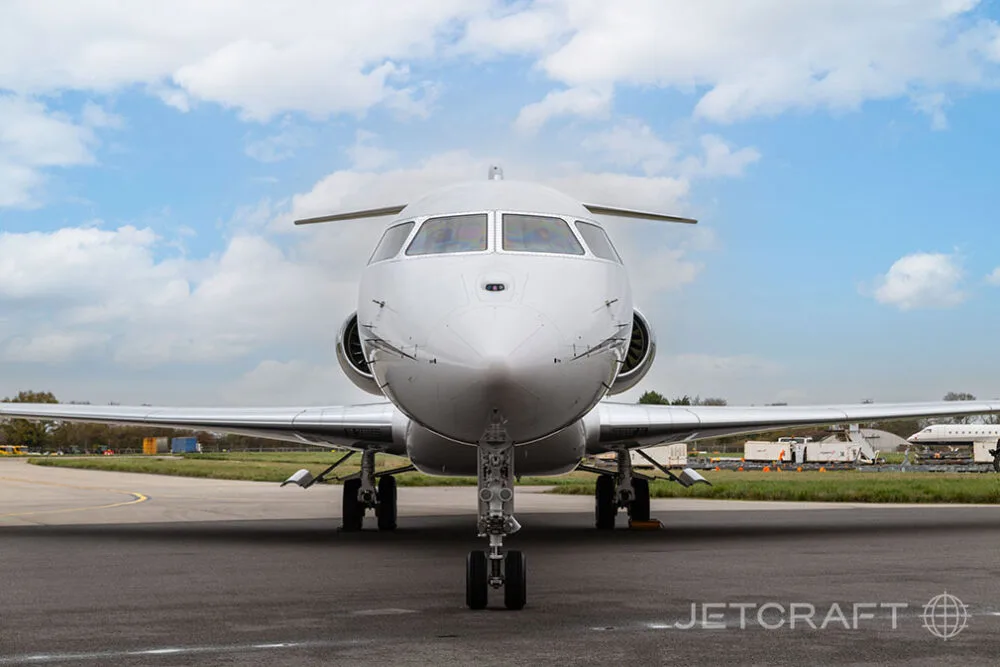 A head-on view of a white Bombardier Global business jet with its landing gear extended on an airfield.