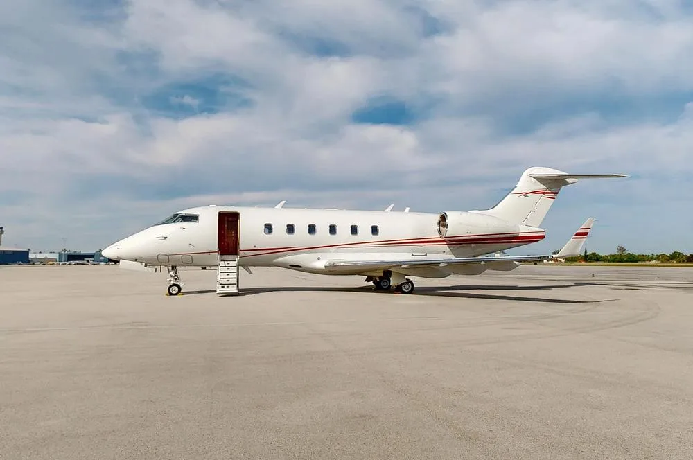 A white business jet with red stripes on the fuselage and tail, parked on a tarmac with its main cabin door open.