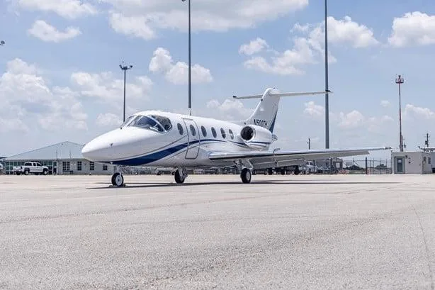 A white business jet with blue stripes, registration N500TH, parked on an airport tarmac under a partly cloudy sky.