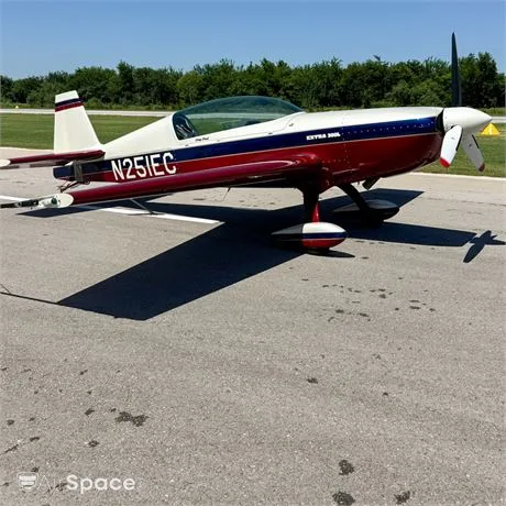 A red, white, and blue Extra 300L aircraft (N251EC) parked on an asphalt tarmac under a clear blue sky.