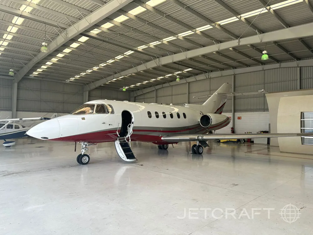 A white and red business jet with its main door open and stairs extended, parked inside a hangar.