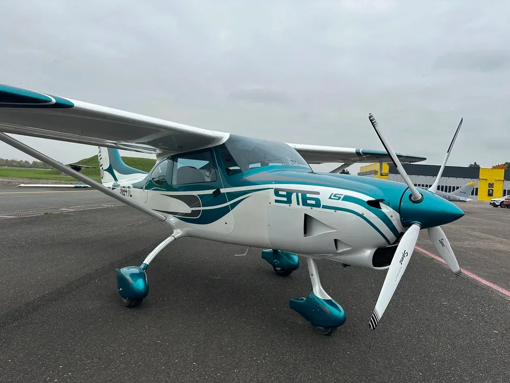 A three-quarter front view of a white and teal Sirius 916 LS aircraft, registration N84TL, parked on an asphalt tarmac on an overcast day.