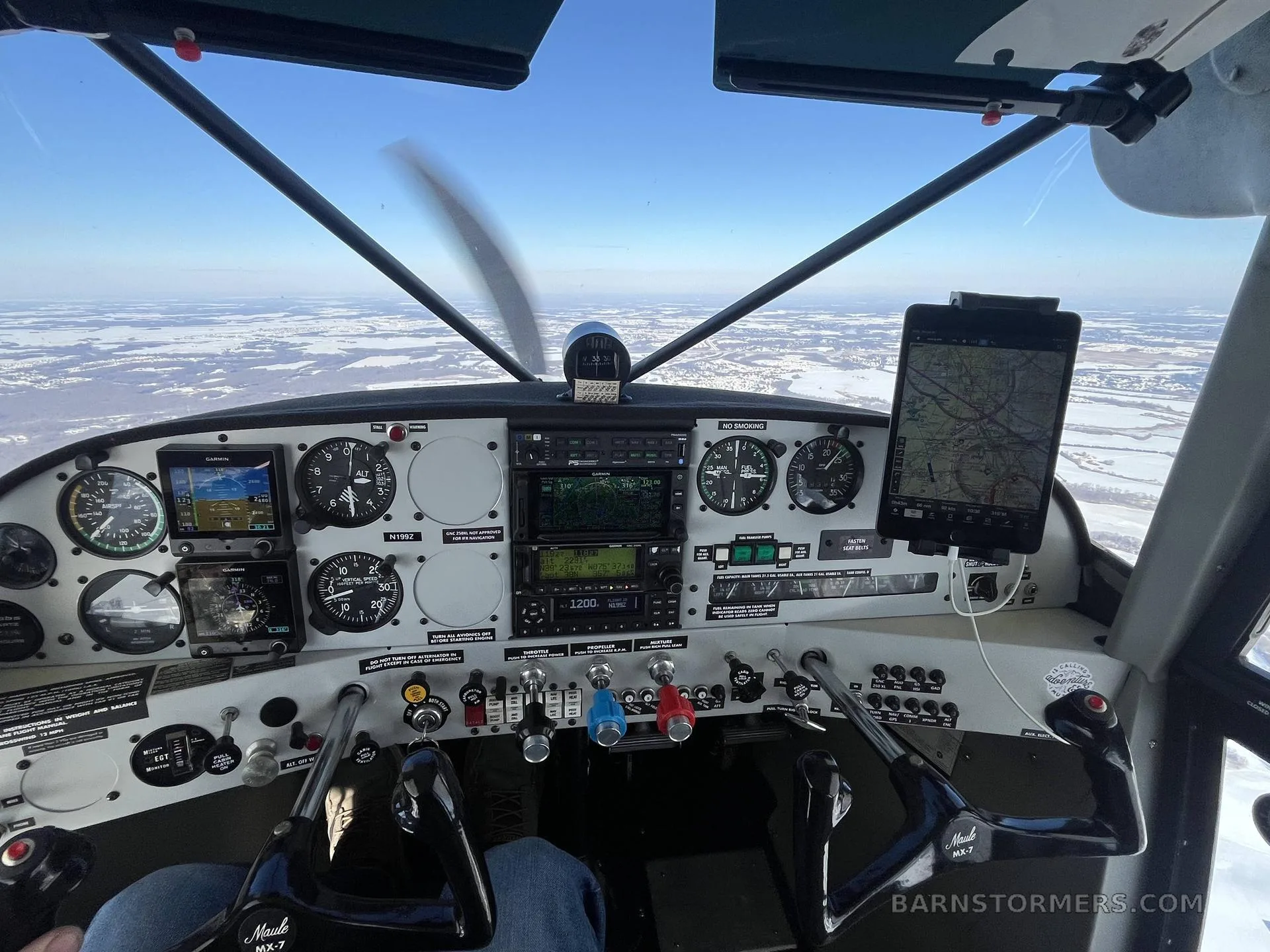 The cockpit of a Maule aircraft shows the instrument panel, controls, and a snowy landscape outside the windshield.