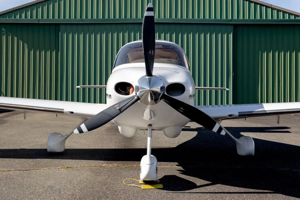 Close-up front view of the white Cirrus SR22 aircraft, showing its propeller and nose gear.